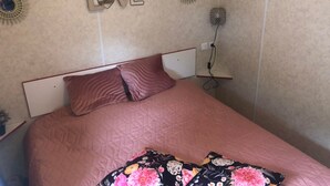 En pænt redt seng med et pink ternet sengetæppe og blomstrede puder, en 'LOVE'-dekoration på væggen og et lille natbord med en lampe.