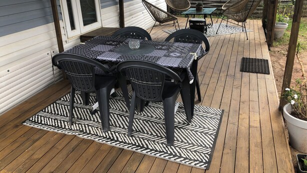 En overdækket terrasse med et bord og stole, et lille bord med en vase samt en potteplante.