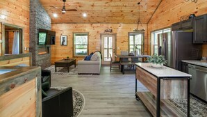 A spacious cabin interior with a stone fireplace, wooden walls, a dining area, and a kitchen with stainless steel appliances. - Allure Woods: View, HotTub, Outdoor Dining & Games (Sevierville)