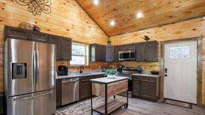 A modern kitchen with wooden walls, stainless steel appliances, and a central island. - Allure Woods: View, HotTub, Outdoor Dining & Games (Sevierville)