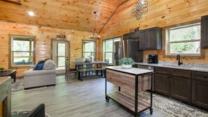 A spacious cabin interior with a wooden ceiling, a dining area, a kitchen with dark cabinets, and large windows. - Allure Woods: View, HotTub, Outdoor Dining & Games (Sevierville)