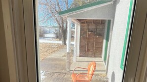Una ventana con vista a un edificio, una puerta de madera y una silla naranja en el exterior.