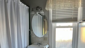 Un baño con lavamanos pedestal blanco, inodoro y ventana con persianas.
