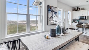 A modern kitchen with large windows, a dining area with a wooden table, and white cabinets. - Chic, waterfront home with on-site golf, pool, wraparound balcony, grill, & W/D (Port Aransas)