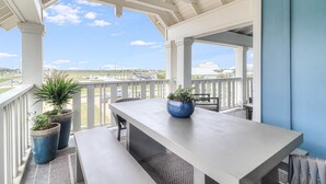 A covered patio with a table and benches, potted plants, and a view of a distant landscape. - Chic, waterfront home with on-site golf, pool, wraparound balcony, grill, & W/D (Port Aransas)
