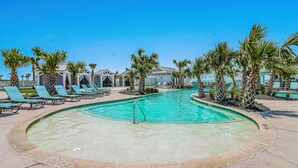 A pool area with lounge chairs and palm trees. - Chic, waterfront home with on-site golf, pool, wraparound balcony, grill, & W/D (Port Aransas)