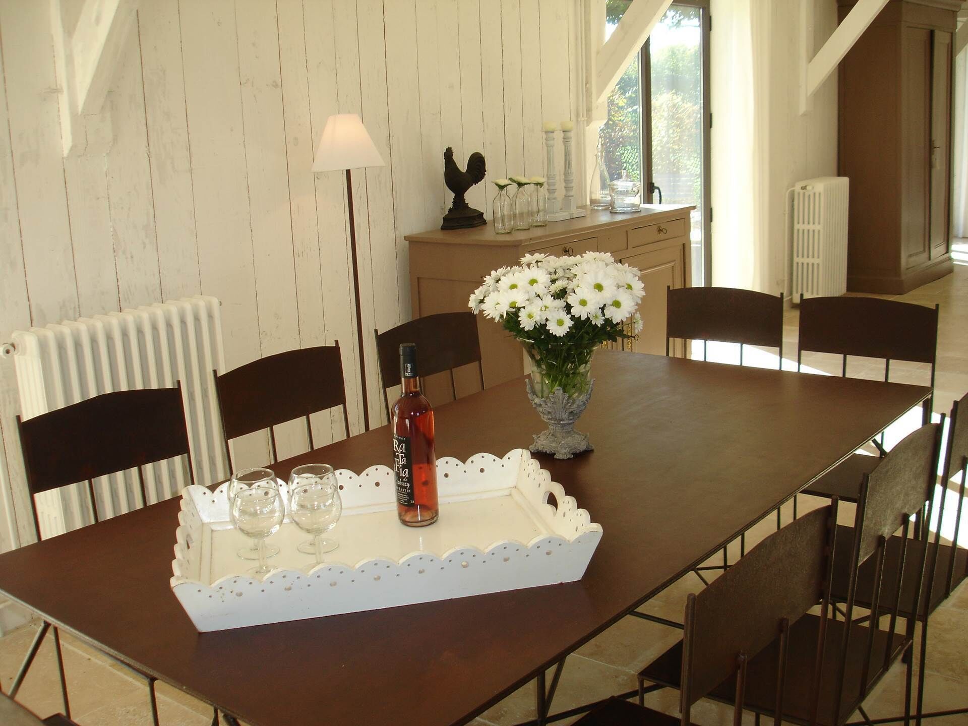 Een eettafel met een fles, glazen en een bloevas.
