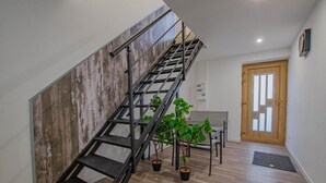 A staircase with a metal handrail, wooden floor, a dining table with chairs, a potted plant, and a wooden door with glass panels.