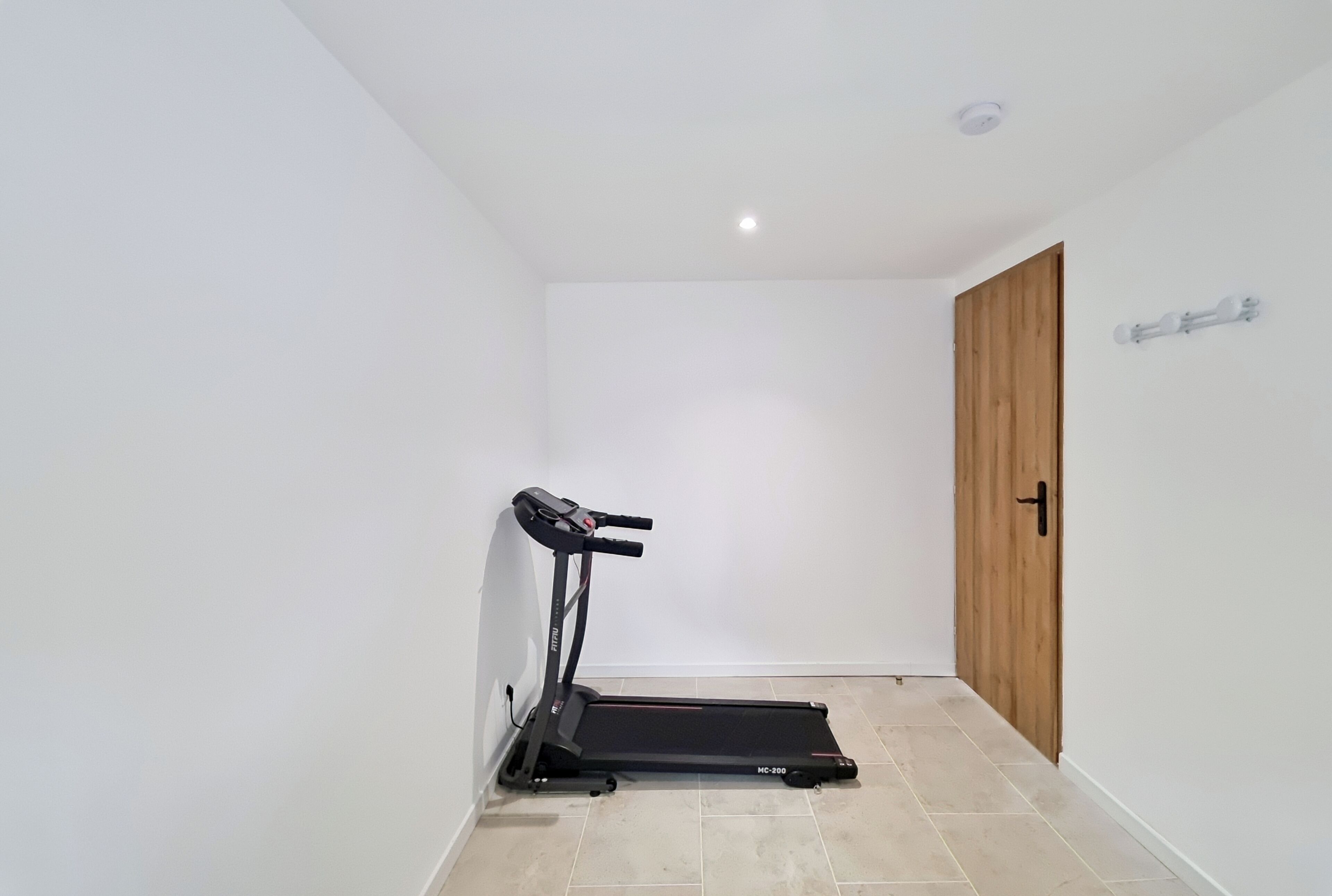Une pièce avec un tapis de course, une porte en bois et un mur blanc.
