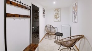 A modern interior with a wooden coat rack, a bench, two wicker chairs, a small table, and wall art.