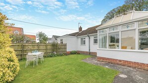 A residential property with a well-maintained lawn, a patio table with chairs, and a white building with large windows. - Discover coastal comfort with your perfect retreat in the heart of Beadnell. (Beadnell, near Chathill)