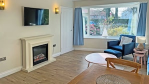 A living room with a fireplace, a television mounted on the wall, a dining table with chairs, and a large window with curtains. - Discover coastal comfort with your perfect retreat in the heart of Beadnell. (Beadnell, near Chathill)