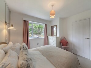 A bedroom with a bed, a dresser, a chair, a window, and a door.