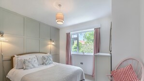 A bedroom with a bed, bedside lamps, a window with curtains, and a chair with a cushion. - Discover coastal comfort with your perfect retreat in the heart of Beadnell. (Beadnell, near Chathill)