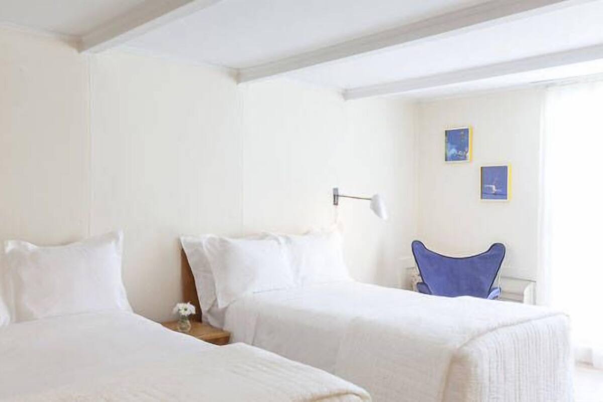 A hotel room with two single beds, a desk, a chair, and a small table.