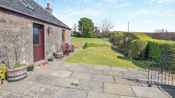 A stone house with a red door, a small garden, and a metal fence.