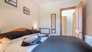 A neatly made bed with a dark blue blanket, a wooden headboard, and two black pillows. There is a framed picture on the wall above the bed and a mirror on the adjacent wall.