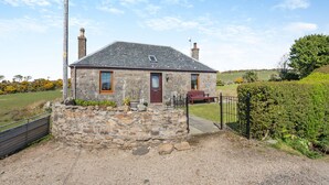 A stone cottage with a sloped roof, a wooden door, and a small porch with a bench.