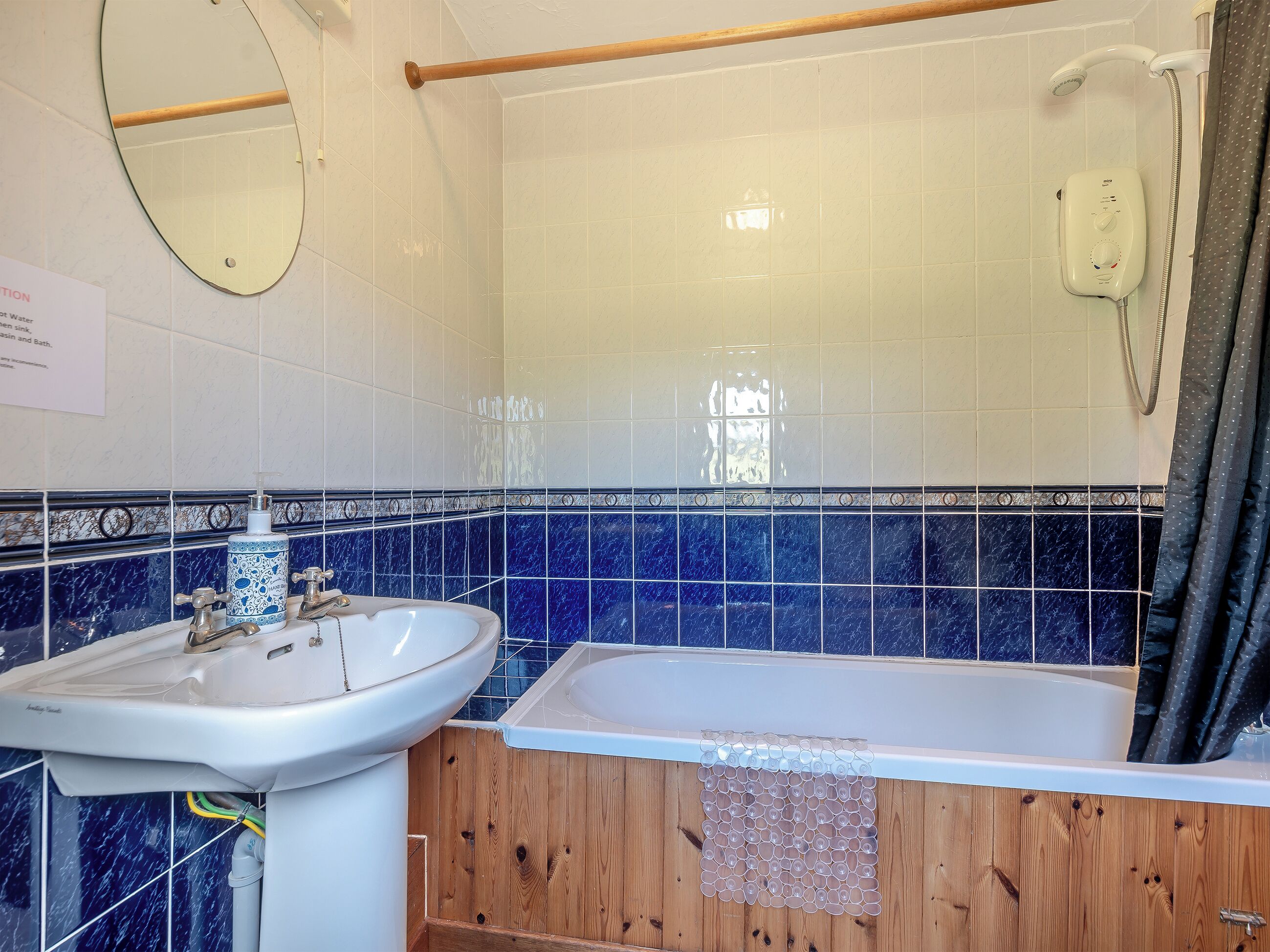 A bathroom with a white sink, a wooden bathtub, and a shower with a handheld showerhead.