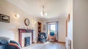 A living room with a fireplace, leather chairs, a television on a wooden stand, and a large window with curtains.