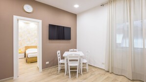 Une chambre à coucher avec un lit, une table de chevet et une commode. On y trouve également un coin repas avec une table et des chaises. Une horloge est fixée au mur.