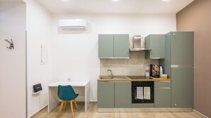 Une cuisine compacte équipée d’un évier, d’une cuisinière et d’un petit réfrigérateur. On y trouve une chaise et un bureau blanc avec un ordinateur.