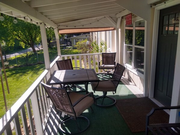 Eine überdachte Terrasse mit Tisch und Stühlen, Blick auf den Garten und eine Tür mit einem Schild.