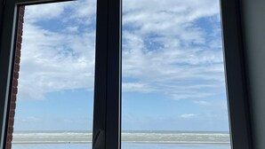 A window with a view of a beach, grassy area, and a wooden fence. - Face MER Pieds Dans L'eau Duplex 4 Chambres 150 M2 8-12 Personnes, Parking ,wifi (Berck)