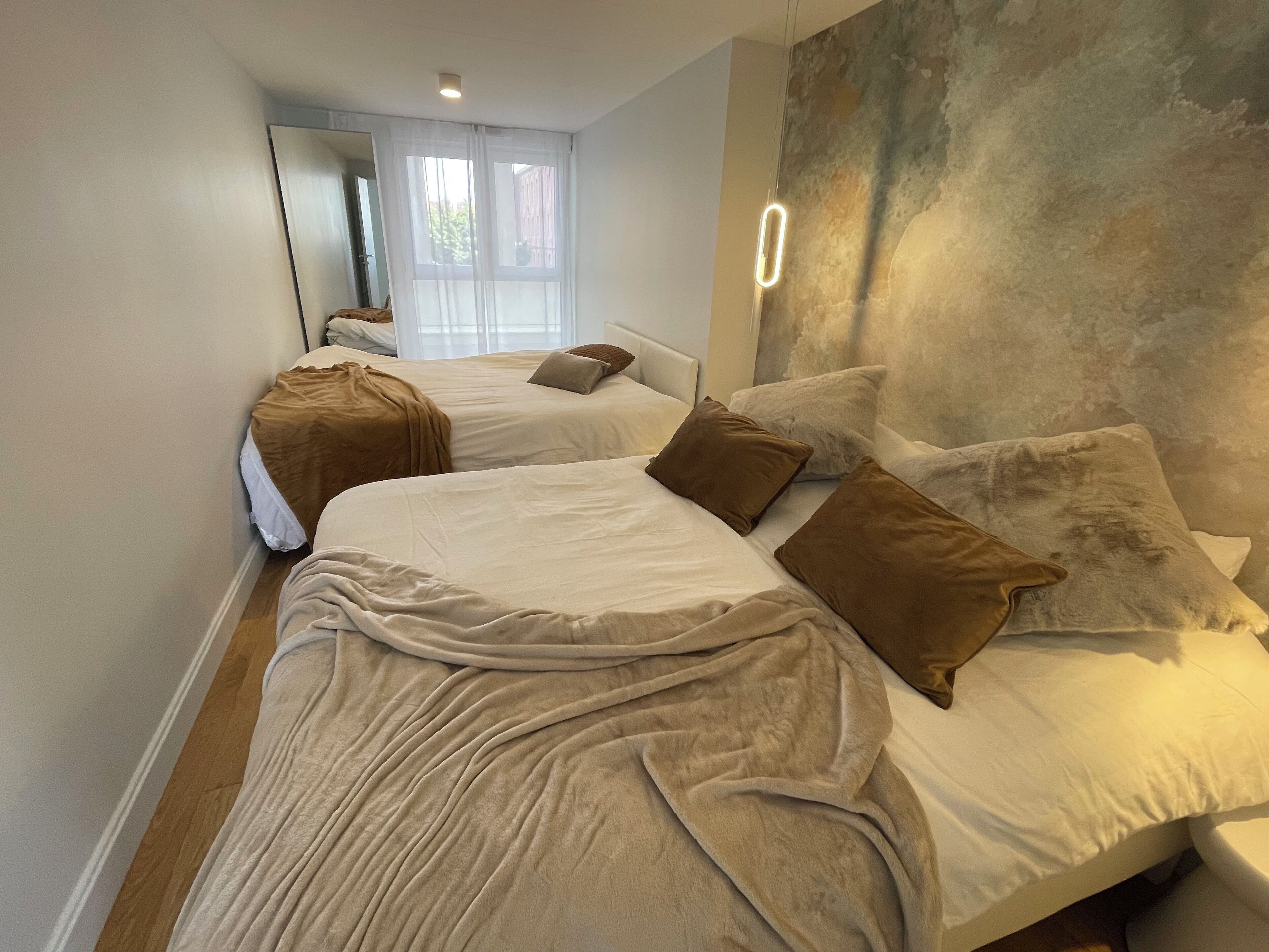 Un dormitorio moderno con dos camas, un espejo grande y una pared con textura.