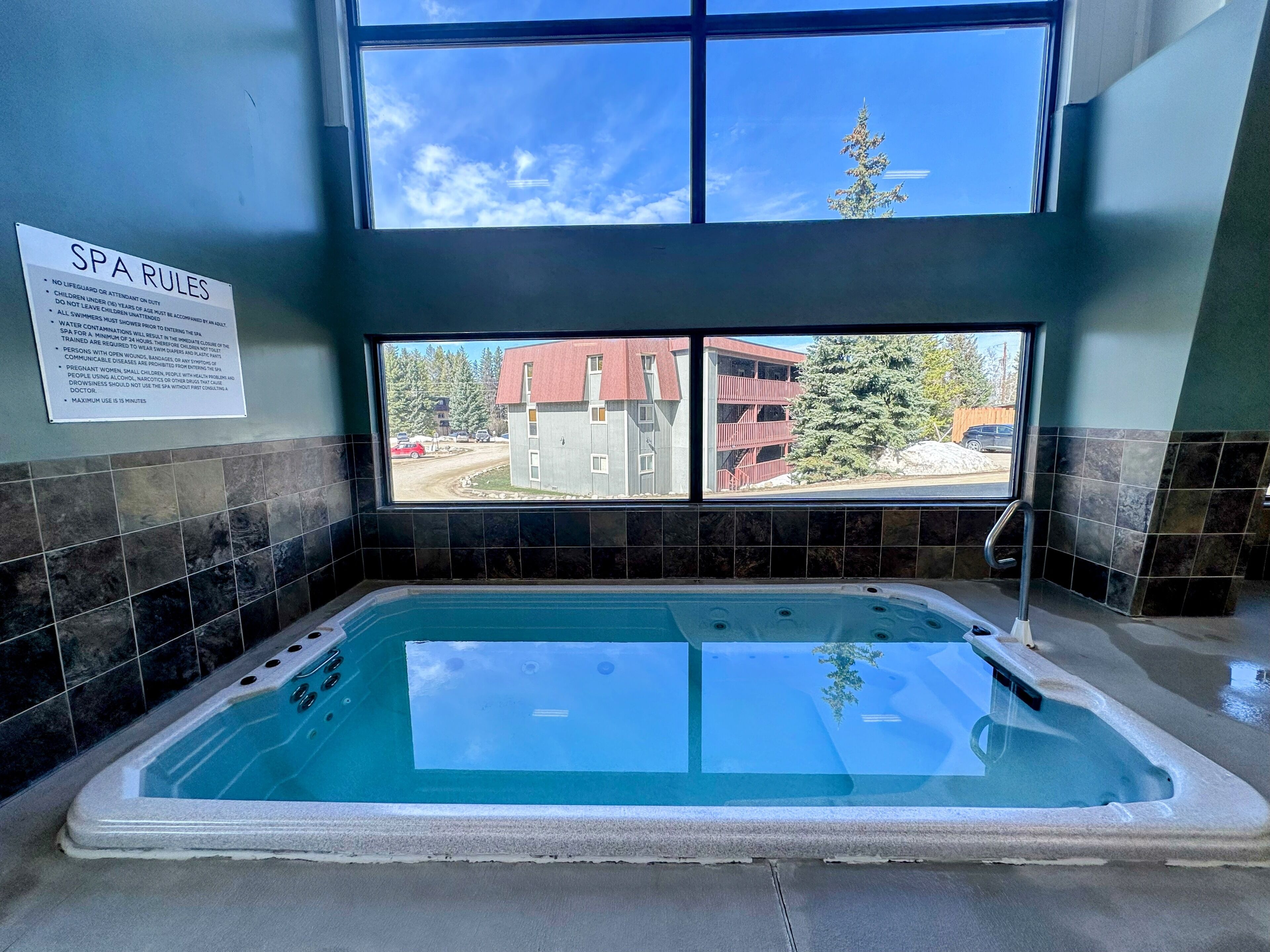 A spa area with a hot tub, a sign detailing spa rules, and a window view of a building and trees.