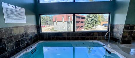 A spa area with a hot tub, a sign detailing spa rules, and a window view of a building and trees.