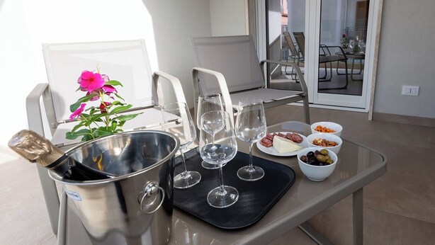 A balcony with a table set for a meal, including a champagne bottle, wine glasses, cheese, olives, and nuts. - Altamarea Sea Apartments (Balestrate)