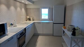 Una cucina moderna con mobili bianchi, forno integrato, macchina da caffè e frigorifero.