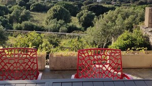 Una terrazza con tavolo e sedie rosse, con vista su un paesaggio costiero con case e vegetazione.