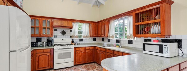 A kitchen with wooden cabinets, a white refrigerator, a stove, a microwave, and a window with curtains.