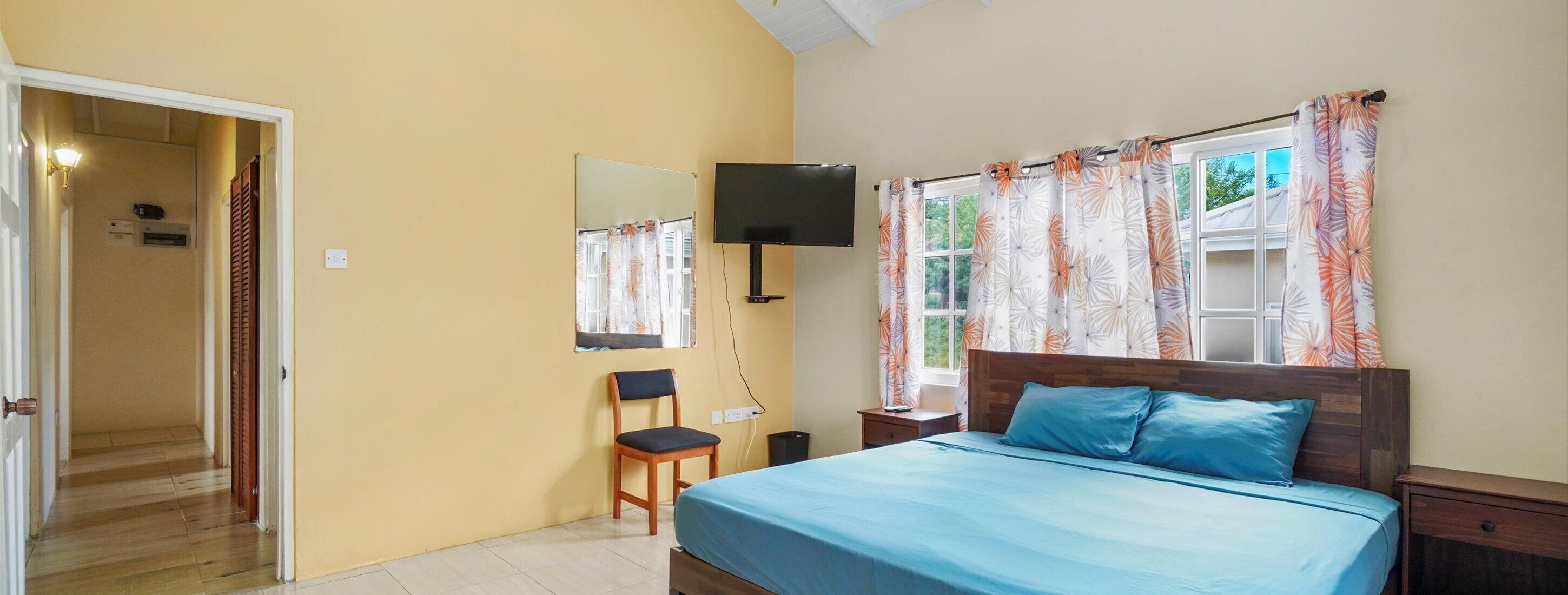 A bedroom with a bed, a desk, a chair, a TV, and a window with curtains.