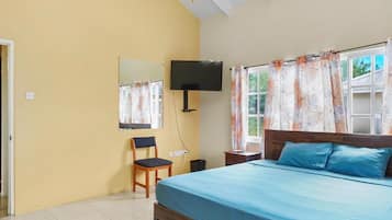 A bedroom with a bed, a desk, a chair, a TV, and a window with curtains.