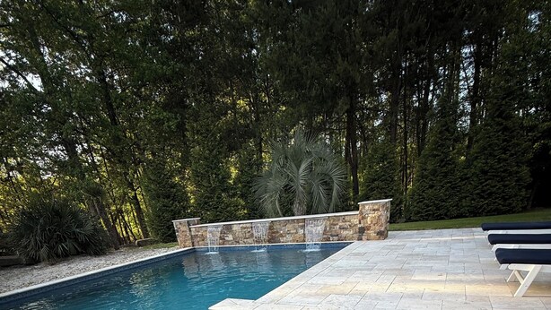 Une piscine rectangulaire agrémentée d’une cascade, entourée de murs en pierre et dotée d’une terrasse en pierre.