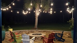 Un espace extérieur aménagé en terrasse, avec des fauteuils Adirondack, un foyer en pierre et des guirlandes lumineuses.