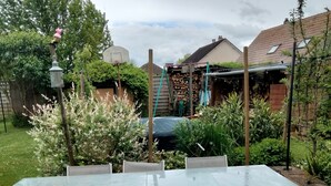 Un jardin avec une table et des chaises en verre, entouré de plantes et d’une clôture en bois.