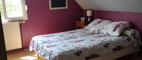 A bedroom with a bed, a window, and a cityscape painting on the wall.