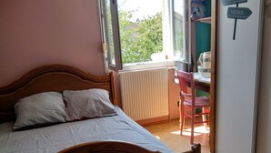 A bedroom with a wooden bed, a radiator, a window, and a desk with a chair.