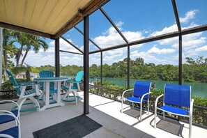 A covered outdoor seating area with chairs and a table, overlooking a body of water and greenery.