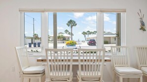A dining area with white chairs and a table, a window with a view of palm trees and houses, and a decorative bird on the wall. - Bayview Oasis on Casey Key with canal view - short walk to private beach! (Nokomis)