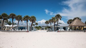 A beachfront hotel with multiple rooms, palm trees, and a thatched-roof structure. - Bayview Oasis on Casey Key with canal view - short walk to private beach! (Nokomis)