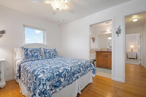 A bedroom with a bed, a ceiling fan, a window, and an open door leading to a bathroom.