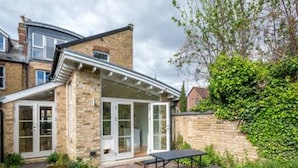 A two-story house with a brick exterior, a front door with glass panels, and a small patio area with a table and bench. - Summertown 4-BR Family Home - Bright & Spacious (Oxford)