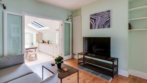 A living room with a sofa, a coffee table, a fireplace, and a TV mounted on the wall. - Summertown 4-BR Family Home - Bright & Spacious (Oxford)