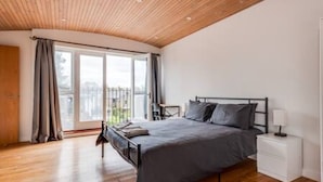 A bedroom with a wooden ceiling, a bed with grey bedding, a bedside table with a lamp, and a window with curtains. - Summertown 4-BR Family Home - Bright & Spacious (Oxford)