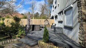 An outdoor patio area with a stone wall, a wooden fence, and a small tree. - Villa touquettoise near the sea (Le Touquet-Paris-Plage)